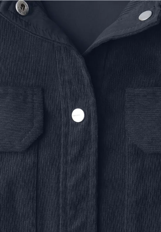 Close-up van een zwarte corduroy jas met borstzakken en zilverkleurige drukknoopsluitingen
