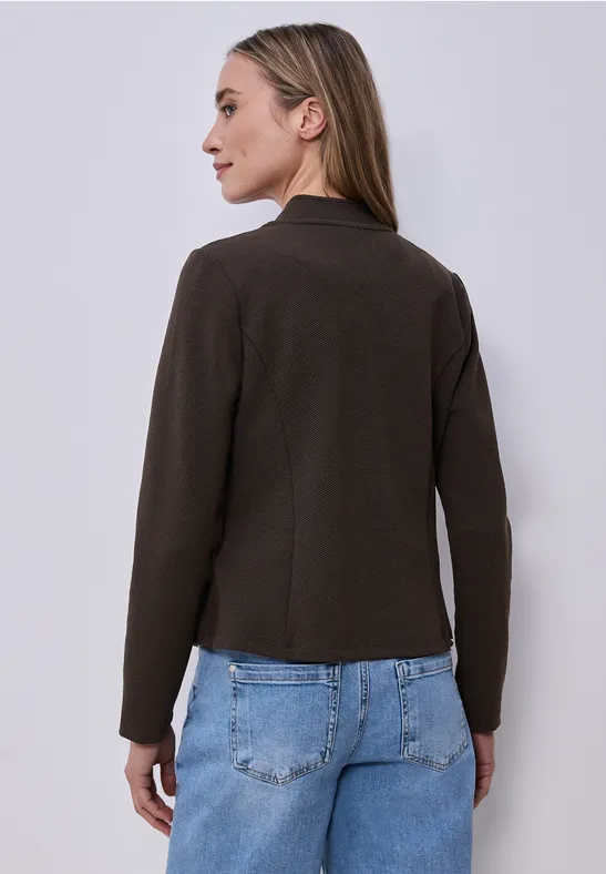 Rückenansicht einer Person mit dunkelbrauner Jacke und blauen Jeans vor neutralem Hintergrund.