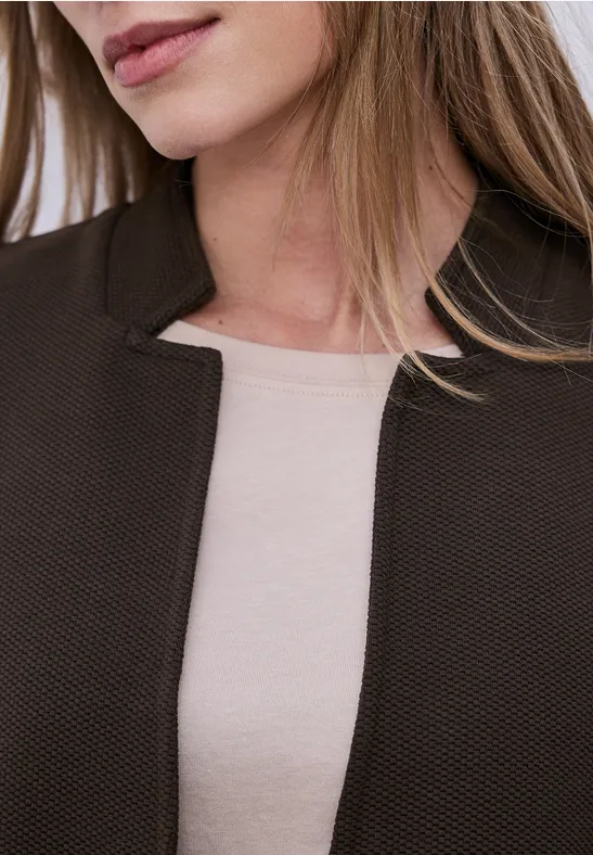 Nahansicht einer Frau, die eine braune Jacke über einem beigefarbenen Top trägt.