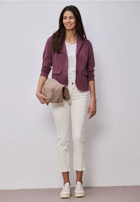 Persoon draagt witte enkellange broek, wit topje, paarse jas, witte sneakers en een beige clutch.
