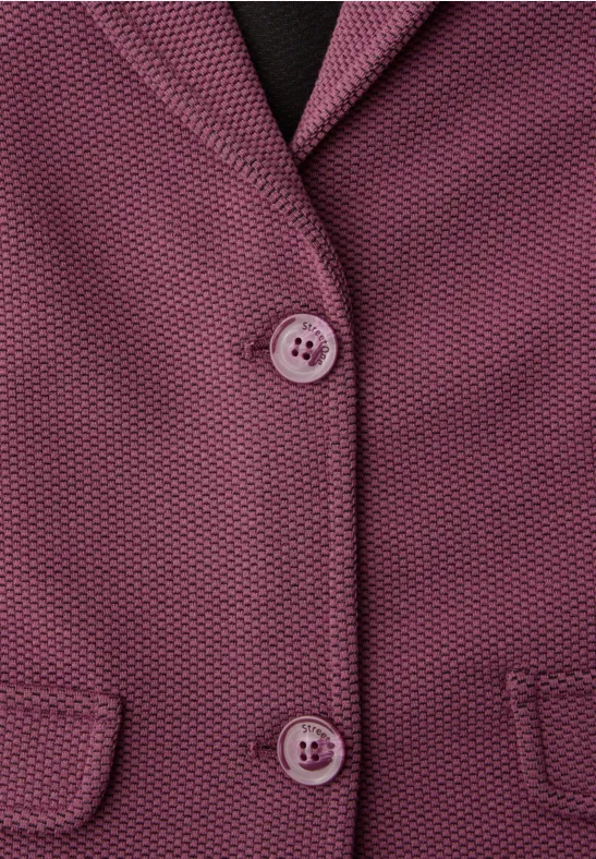 Close-up van een paarse, gestructureerde blazer met twee knopen en kleine klepzakken.