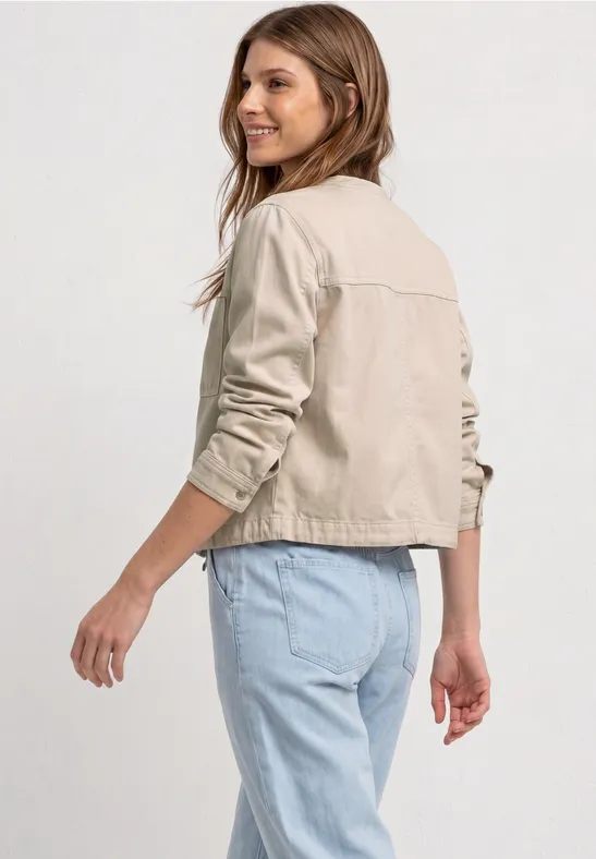 Personne de dos, porte une veste beige et un jean clair sur fond blanc.