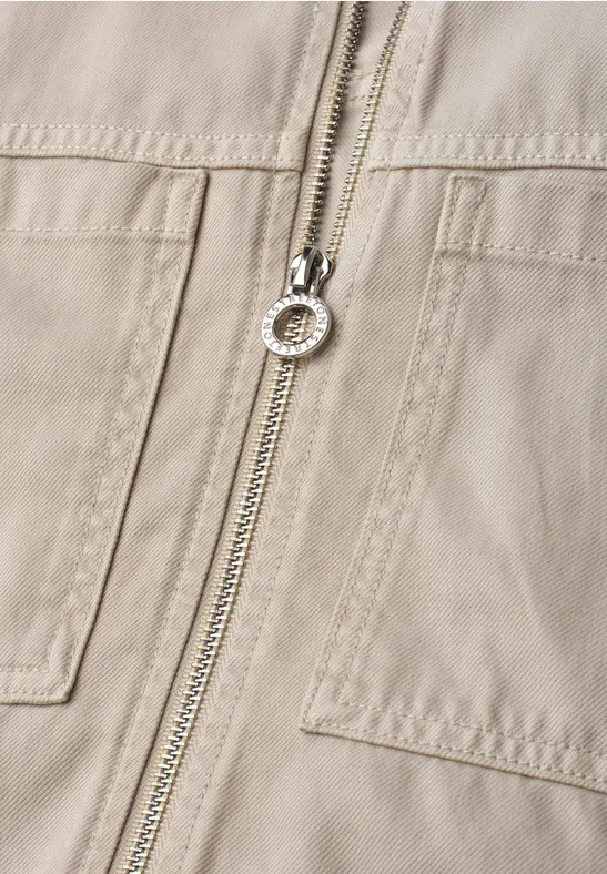 Gros plan d'une veste beige avec fermeture éclair et poches plaquées.
