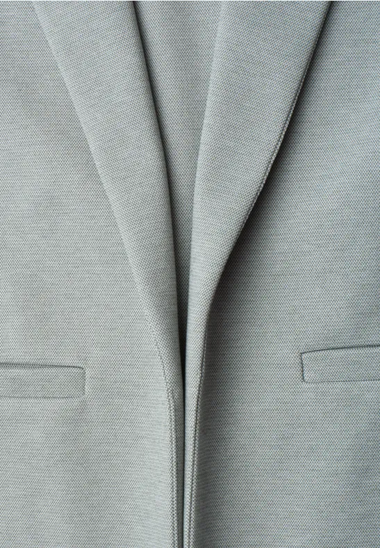 Close-up van een lichtgrijze blazer met subtiele plooien en zakken.