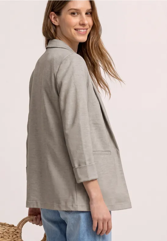 Vrouw met lichtgrijze blazer, losse pasvorm, zijaanzicht tegen lichte achtergrond.
