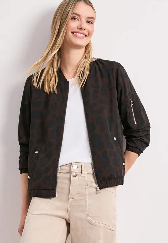 Modell trägt beige Hose und dunkelbraune Bomberjacke mit Herzmuster.