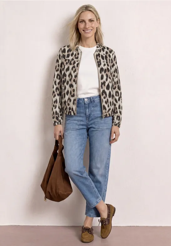 Vrouw in leopardprint jasje, wit shirt, blauwe jeans, bruine tas en bruine loafers.
