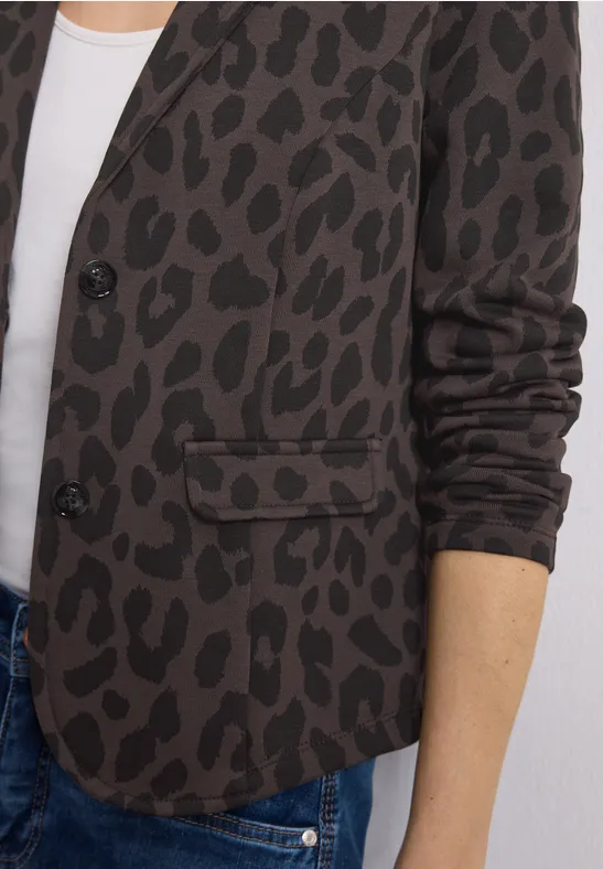 Veste marron à motifs léopard noirs portée sur un top blanc et un jean.