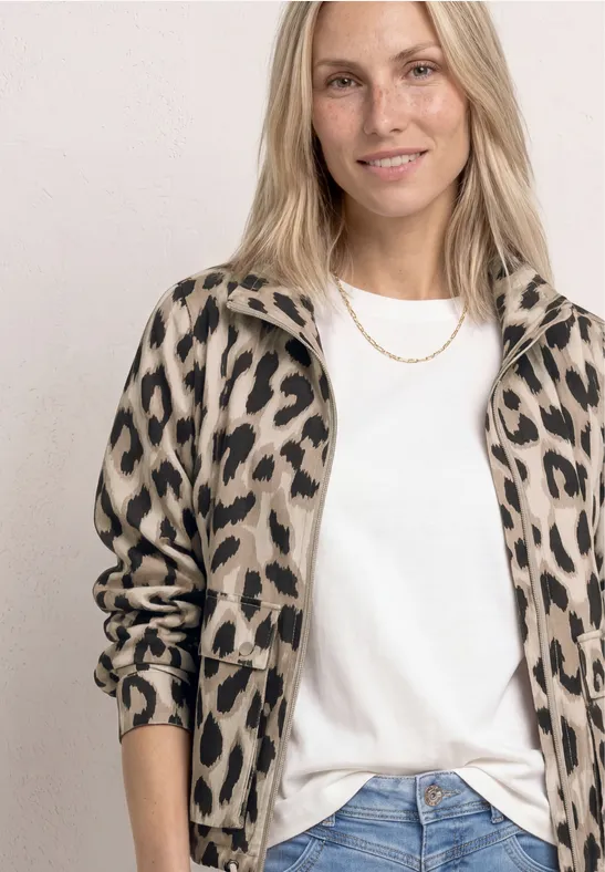 Frau mit Leopardenjacke, weißem T-Shirt und Jeans. Blond, Halskette, Gesicht unscharf.