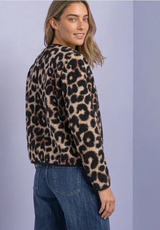 Femme blonde portant un pull léopard et un jean, souriante et regardant par-dessus son épaule.