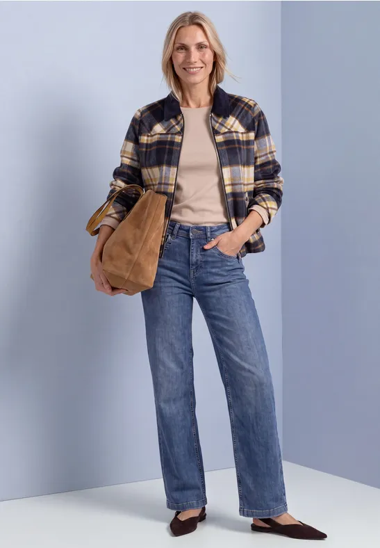 Vrouw lacht in ruitjesjacket, beige top, wijde jeans met bruine tas.