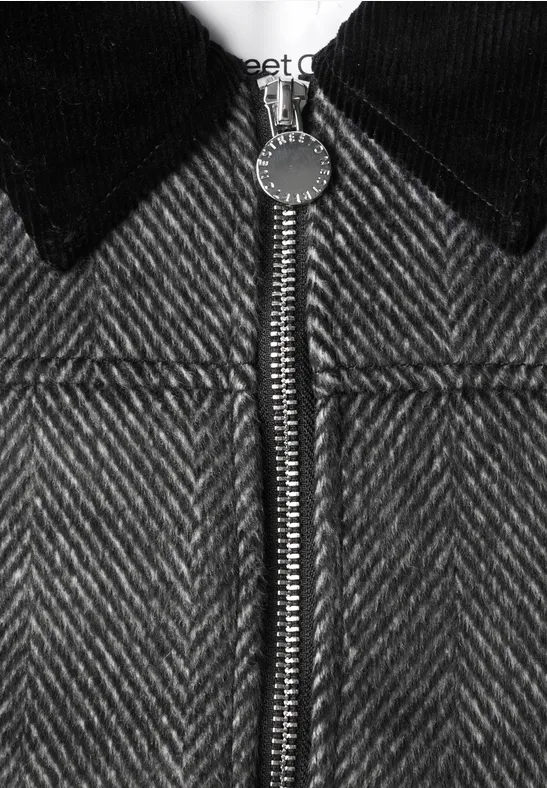 Nahaufnahme einer Jacke aus Hahnentritt-Stoff mit silbernem Reißverschluss und schwarzem Kragen.