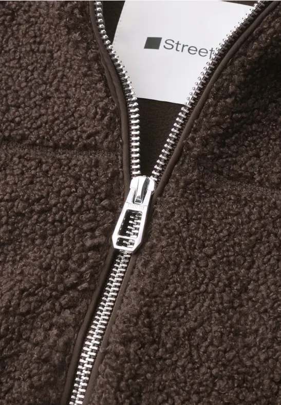 Nahaufnahme eines braunen Teddy-Fleecejacke mit silbernem Reißverschluss und sichtbarem weißen Label 'Stree'.