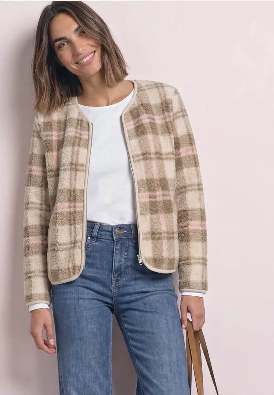 Vrouw lachtend in kort geruit blazer, wit topje, blauwe jeans, met bruine handtas.