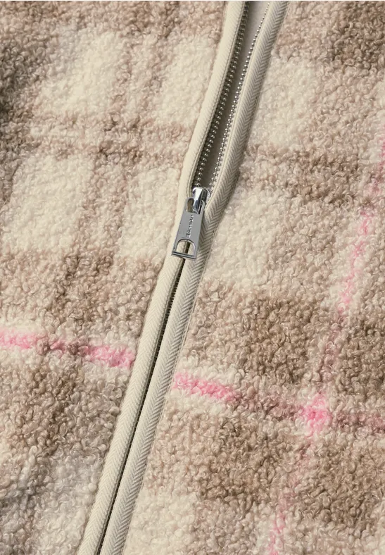 Close-up van een grijs-beige ritssluiting op bruin geruit wollen stof met subtiele roze strepen.