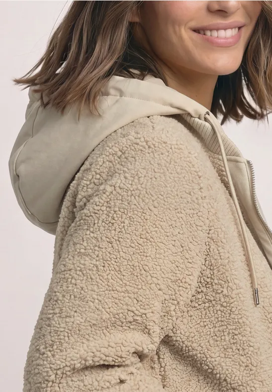 Close-up van een vrouw in een beige teddyfleecejas met capuchon.
