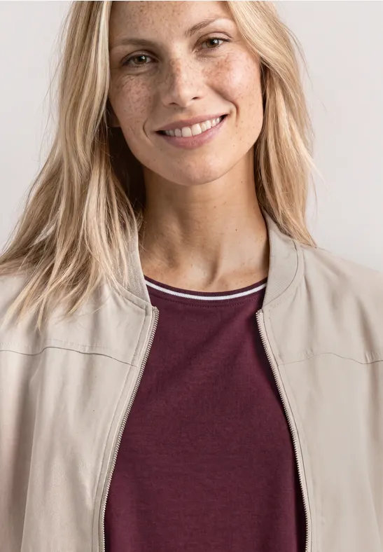 Personne blonde vue des épaules, portant une veste beige et un t-shirt bordeaux.