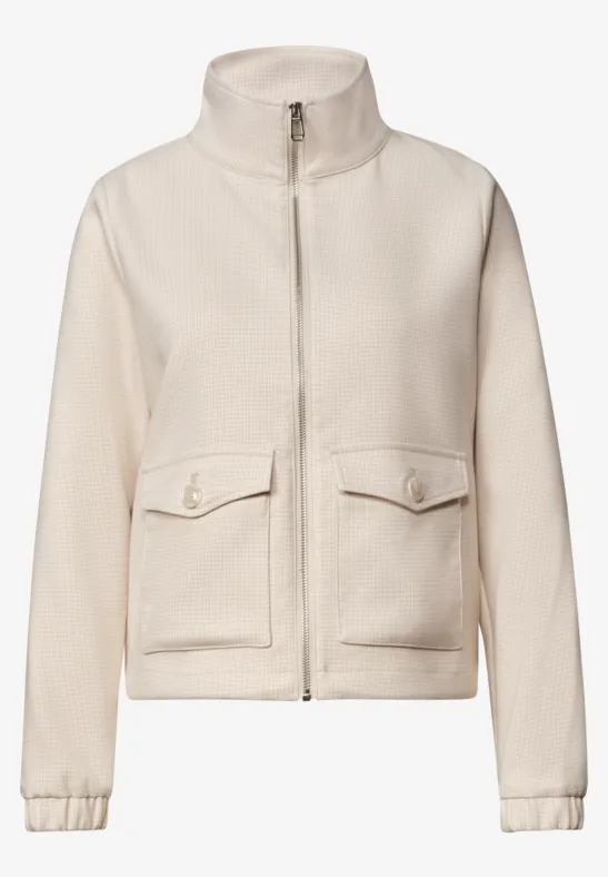 Veste polaire beige à col montant, fermeture éclair et poches plaquées.