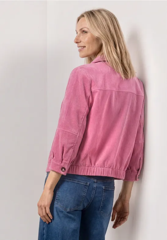 Frau von hinten in rosa Jacke und blauen Jeans vor neutralem Hintergrund.