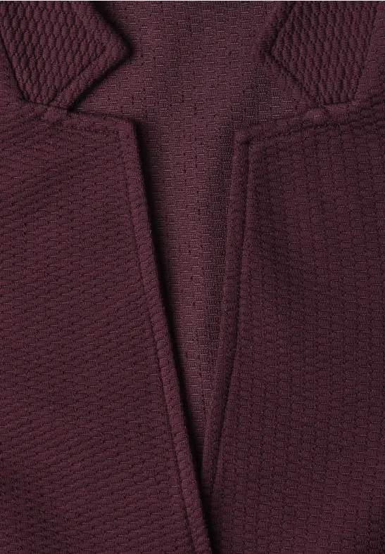 Gros plan sur un pull en maille bordeaux à col en V avec texture tissée.