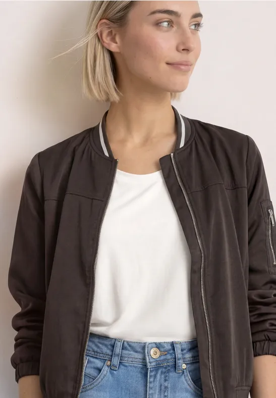 Femme aux cheveux blonds portant une veste bomber noire, un T-shirt blanc et un jean.