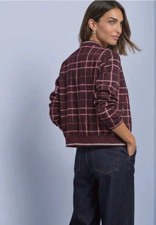 Frau trägt karierte Bomberjacke und Jeans, Blick über die Schulter, Rückansicht.