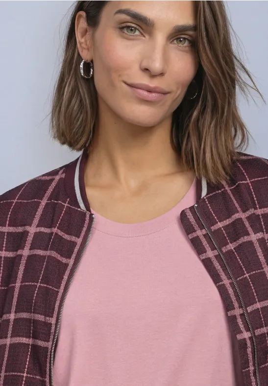 Porträt einer Frau mit braunen Haaren, die ein rosa Top und eine karierte Jacke trägt.