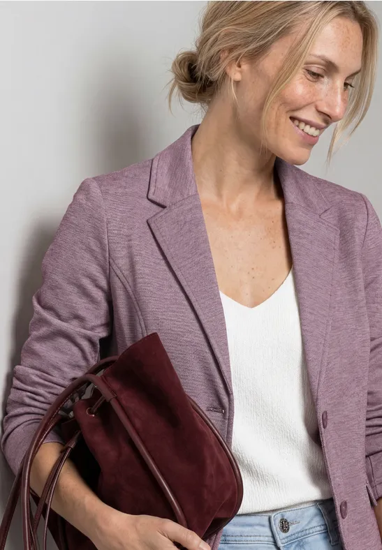 Eine Person mit unkenntlichem Gesicht trägt einen fliederfarbenen Blazer, eine weiße Bluse und eine weinrote Tasche.