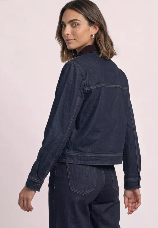 Frau trägt dunkle Denim-Jacke und passende Jeans in schlichtem, modischem Look.