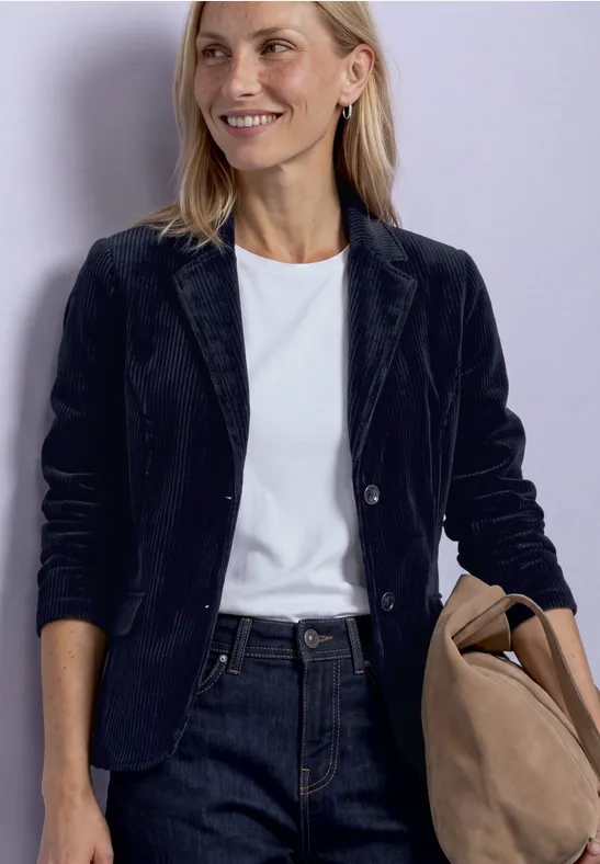 Vrouw in zwarte blazer, wit shirt en spijkerbroek met tas in hand.
