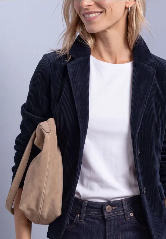 Vrouw met wit T-shirt, donker corduroy colbert en beige suède tas.