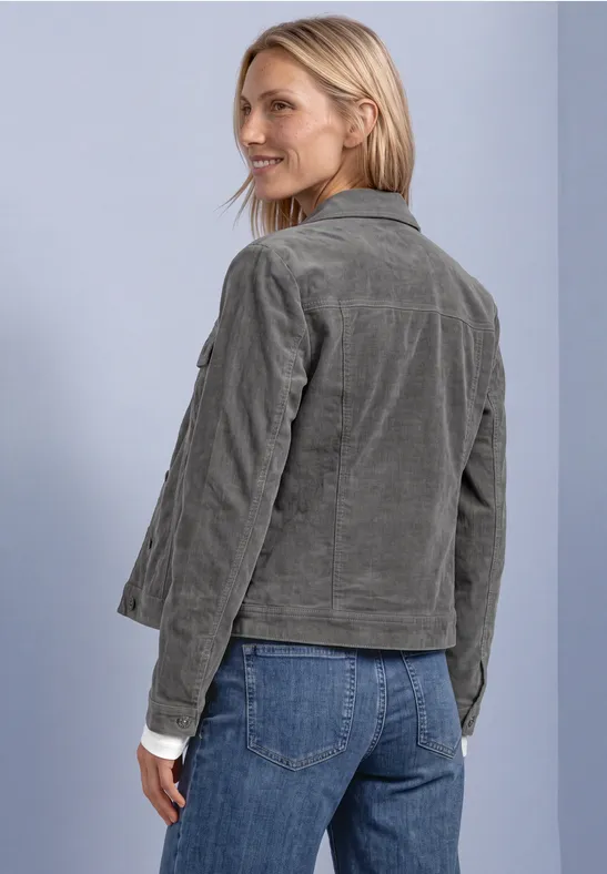 Frau in graugrüner Cordjacke und Jeans, schaut über die Schulter