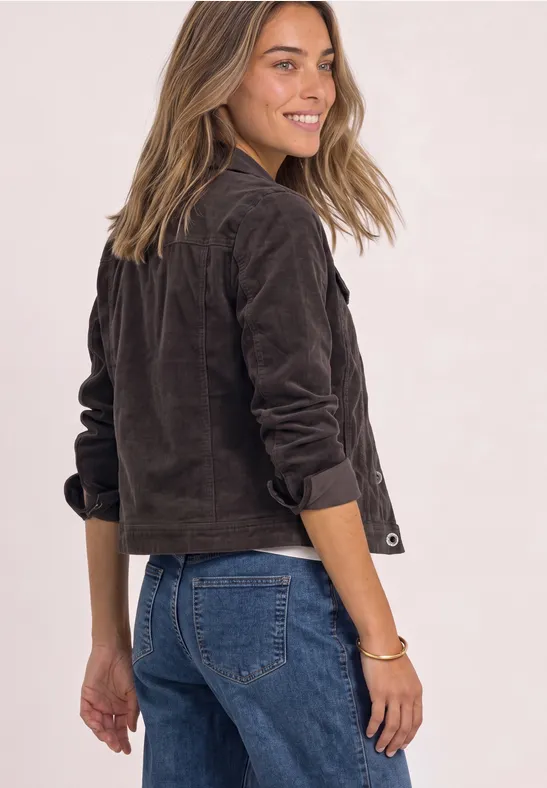 Frau blickt über die Schulter, trägt braune Jacke und blaue Jeans, lächelnd