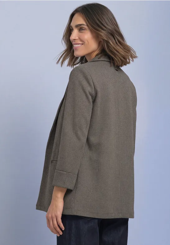 Femme aux cheveux bruns, veste kaki, souriant de profil devant un fond clair.
