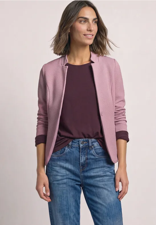 Femme en tenue décontractée portant une veste rose et un jean sur fond clair.