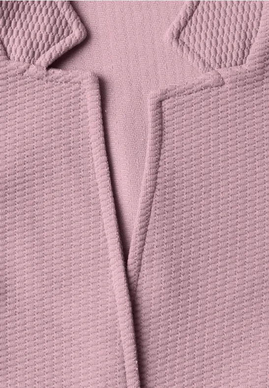 Gros plan d’un blazer en tissu rose texturé, montrant le col et les revers.