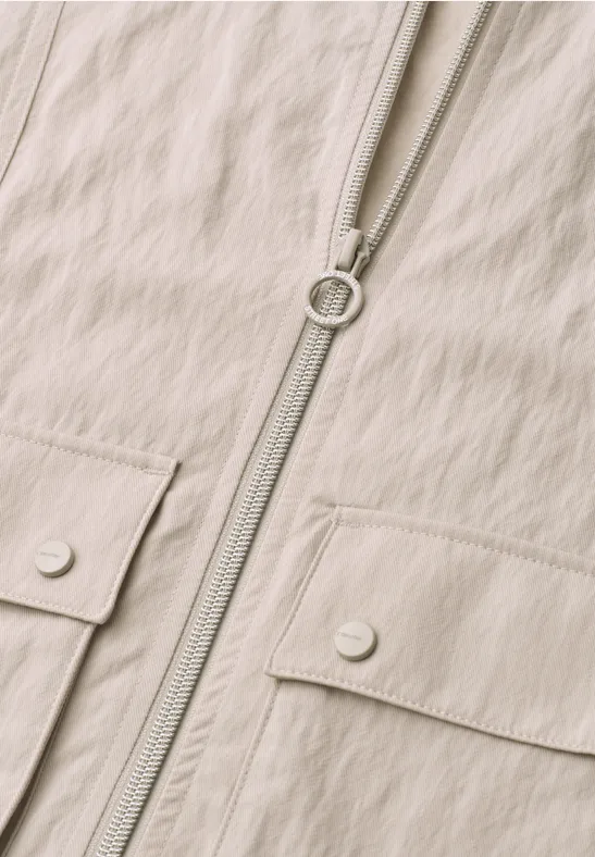 Beige Jacke mit durchgehendem Reißverschluss und zwei Klappentaschen mit Druckknöpfen.