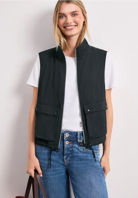 Femme en gilet matelassé noir sur t-shirt blanc, jean bleu et sac à main.