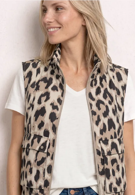 Femme en t-shirt blanc à col V et gilet sans manches imprimé léopard sur fond neutre.