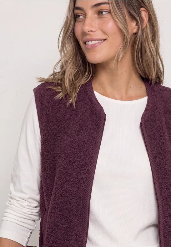 Eine lächelnde Frau im weißen Langarmshirt und lila Fleece-Weste