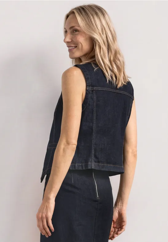 Vue arrière : personne en veste en jean sans manches et jupe assortie, fond épuré, visage flou