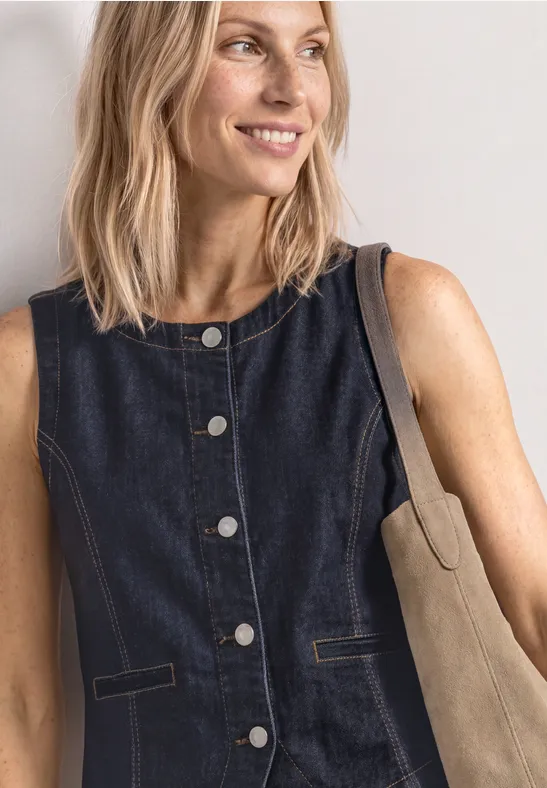 Femme en gilet en jean bleu foncé sans manches avec sac beige sur fond clair.