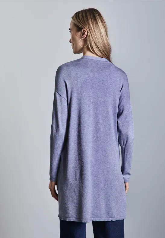 Frau mit langen Haaren trägt lilafarbenen langen Pullover, steht mit dem Rücken zur Kamera.