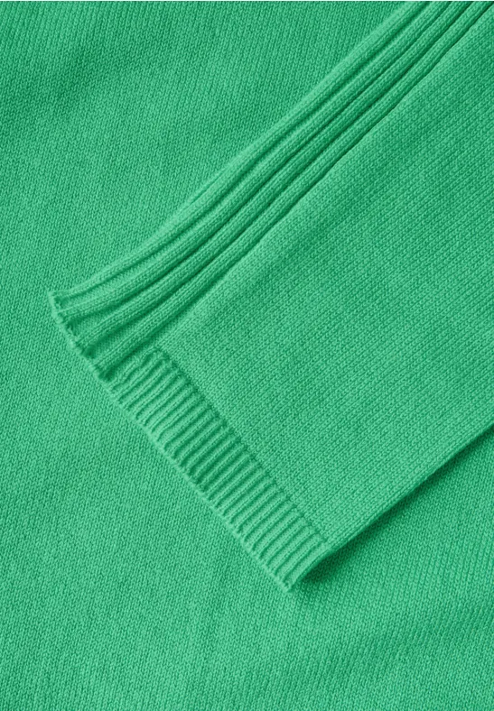 Detail eines grünen Strickpullovers mit geripptem Ärmelbündchen.