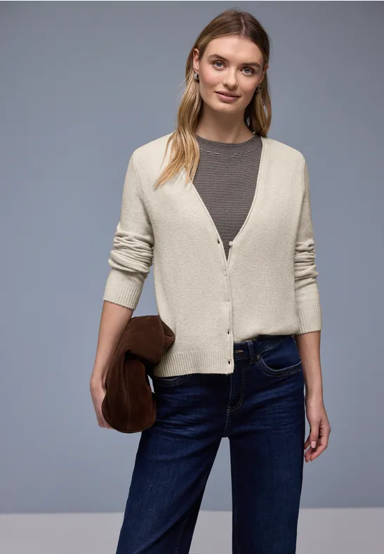 Eine Frau trägt beigen Cardigan, graues Shirt, dunkelblaue Jeans und braune Clutch.