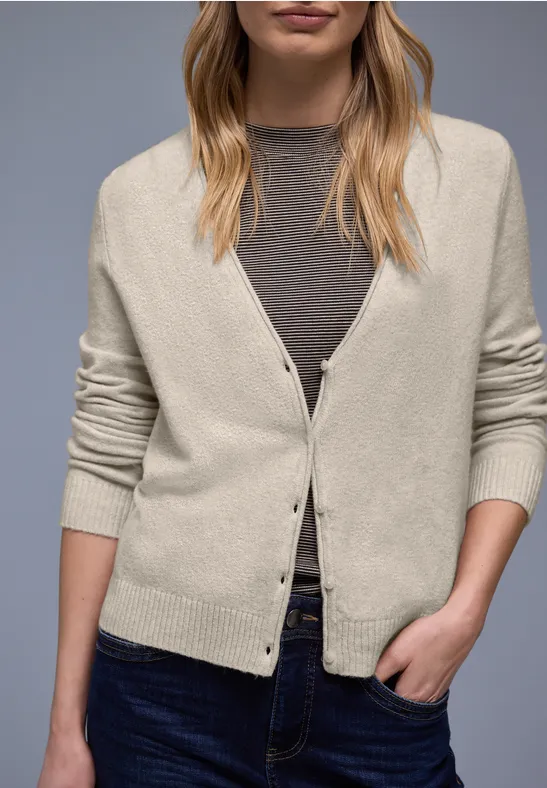 Eine Frau trägt eine beige Strickjacke über einem grauen Top und Jeans.