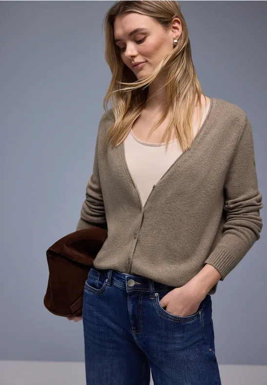 Eine Person trägt einen beigefarbenen Cardigan, weißes Top, blaue Jeans und eine braune Tasche.