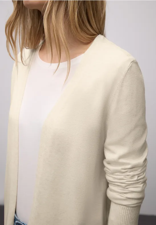 Een persoon draagt een crèmekleurig vest over een wit T-shirt