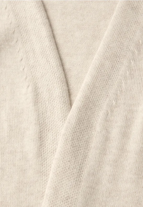 Close-up van een beige gebreide trui met V-hals, zachte structuur.