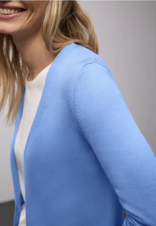 Nahaufnahme einer lächelnden Frau in hellblauer Strickjacke und weißem Shirt.